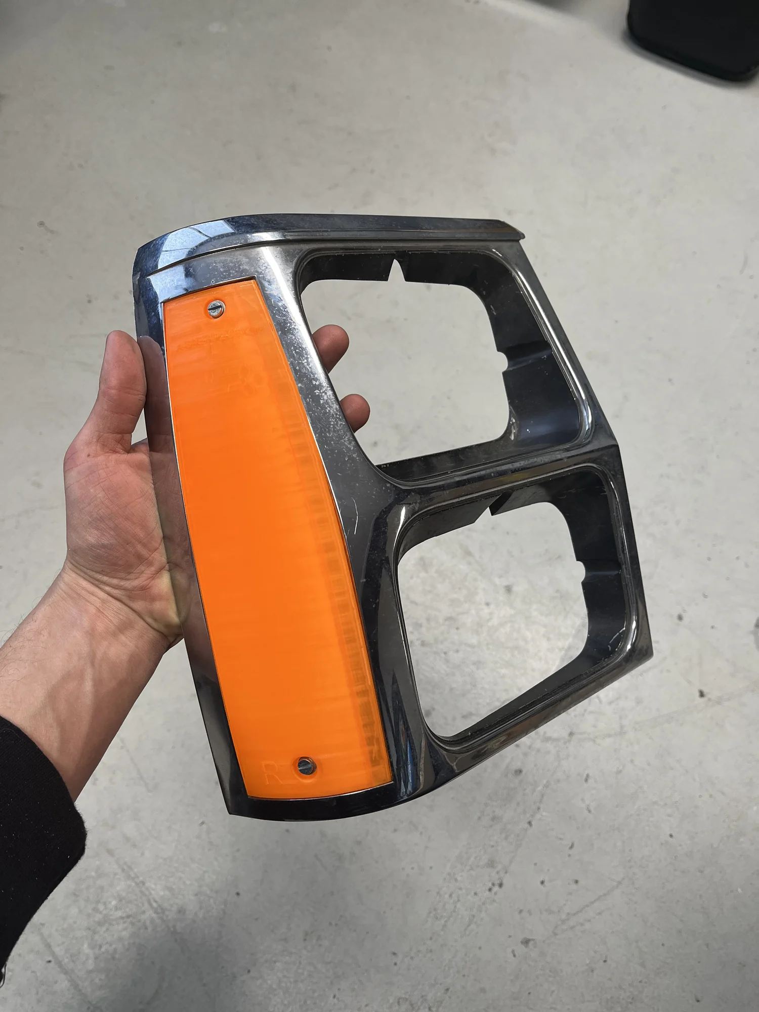 Een nieuw gemaakte oranje knipperlichtlens in de originele verchroomde rand, in de hand gehouden