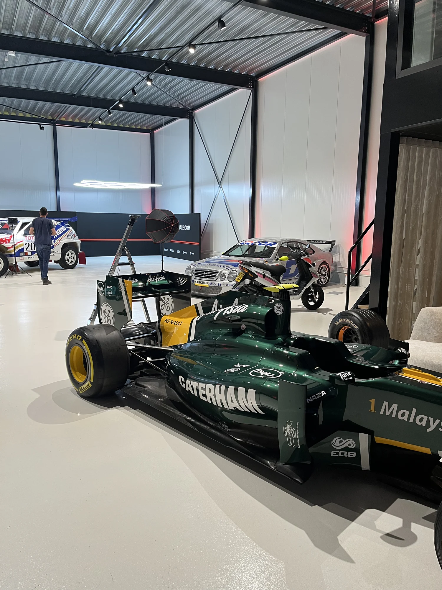 Een groene Caterham Formule 1-auto in een showroom met andere raceauto’s