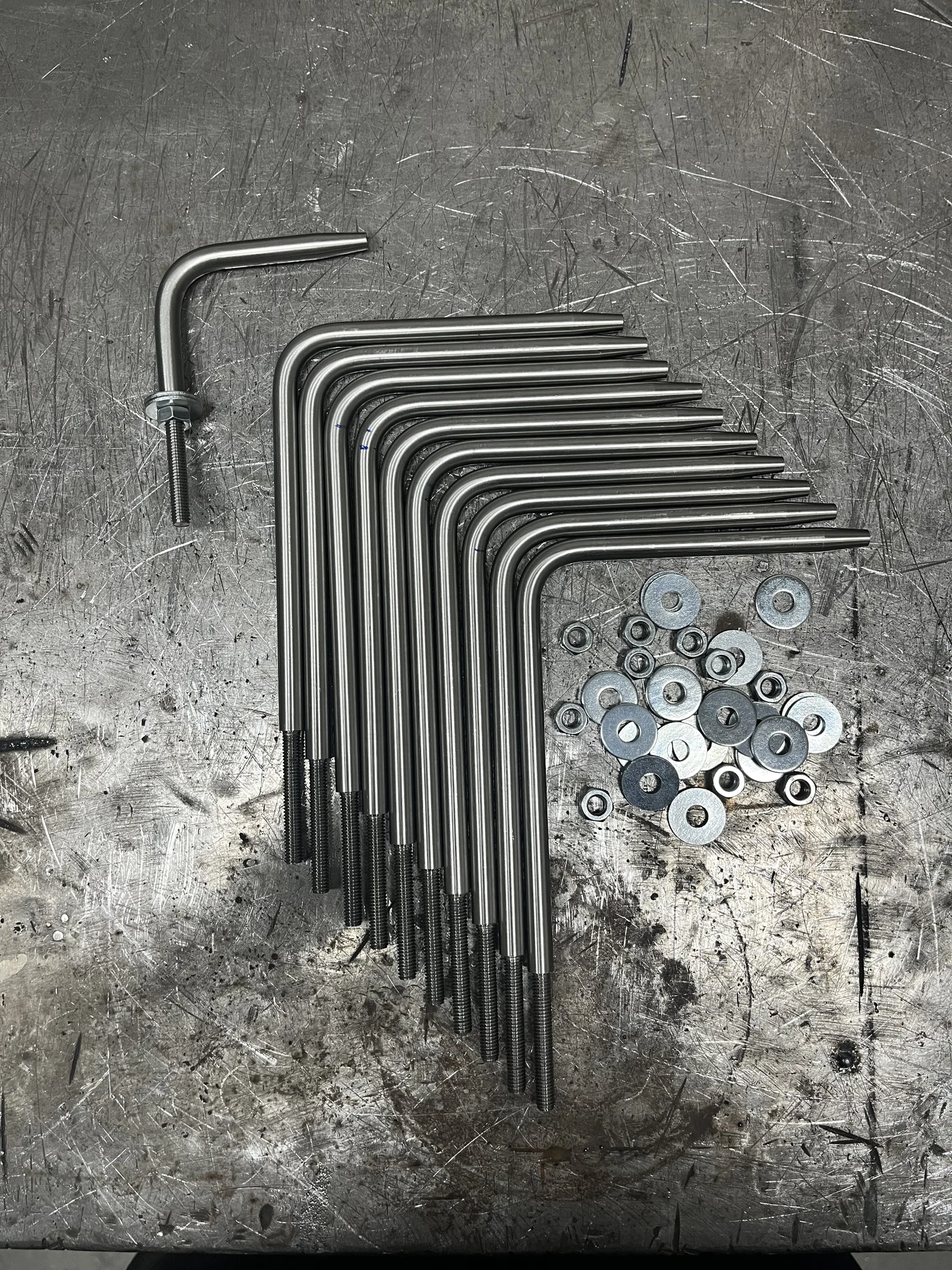 Een rij gebogen metalen buisjes met schroefdraad en ringen op een werkbank
