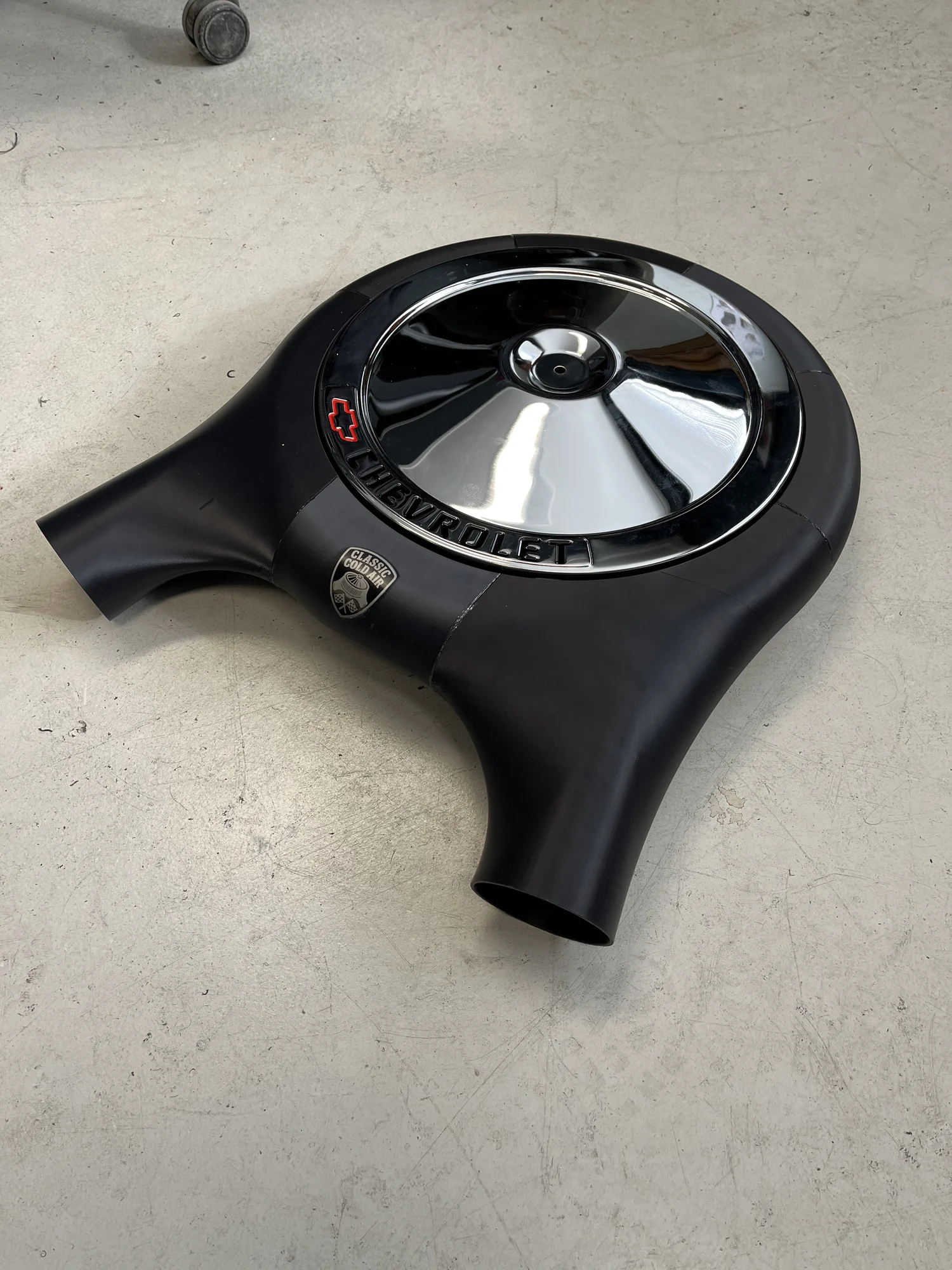 Een zwarte cold air intake met een verchroomd Chevrolet-filterdeksel