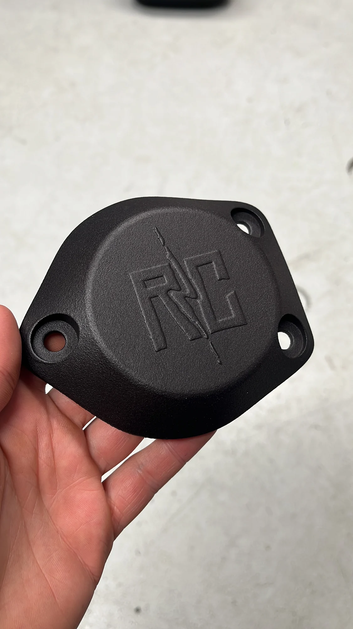 Een zwarte afdekplaat met het Rico Customs-logo, in de hand gehouden