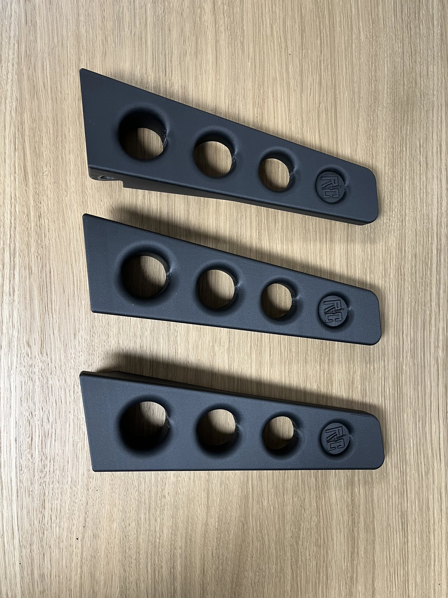 Drie zwarte gaspedalen met drie gaten en het Rico Customs-logo, op een houten tafel